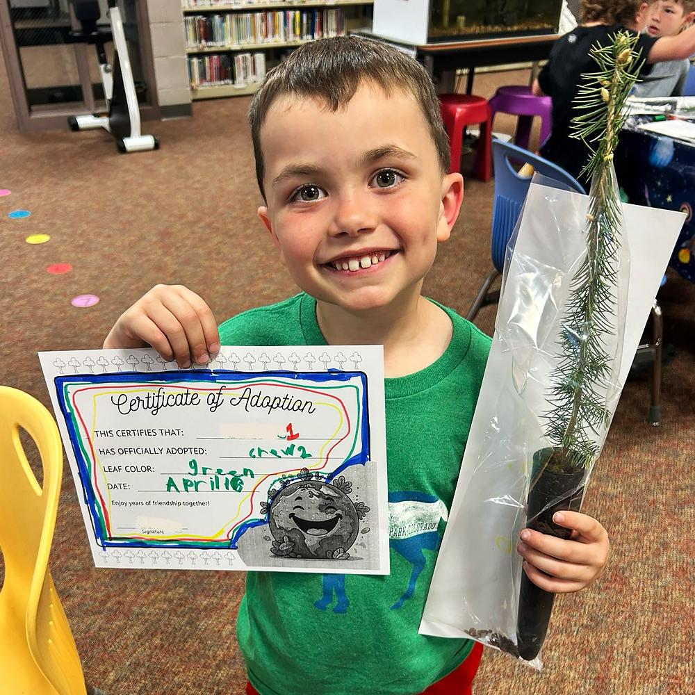 Picture of a little boy, in a classroom, holding a tree sapling and an adoption certificate.