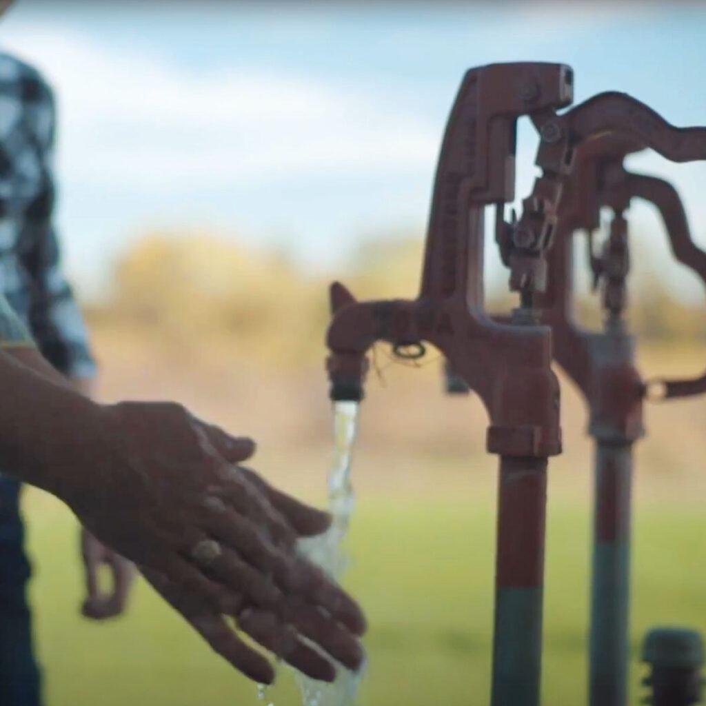 Close-up picture of a person washing their hands underneath a water pump.